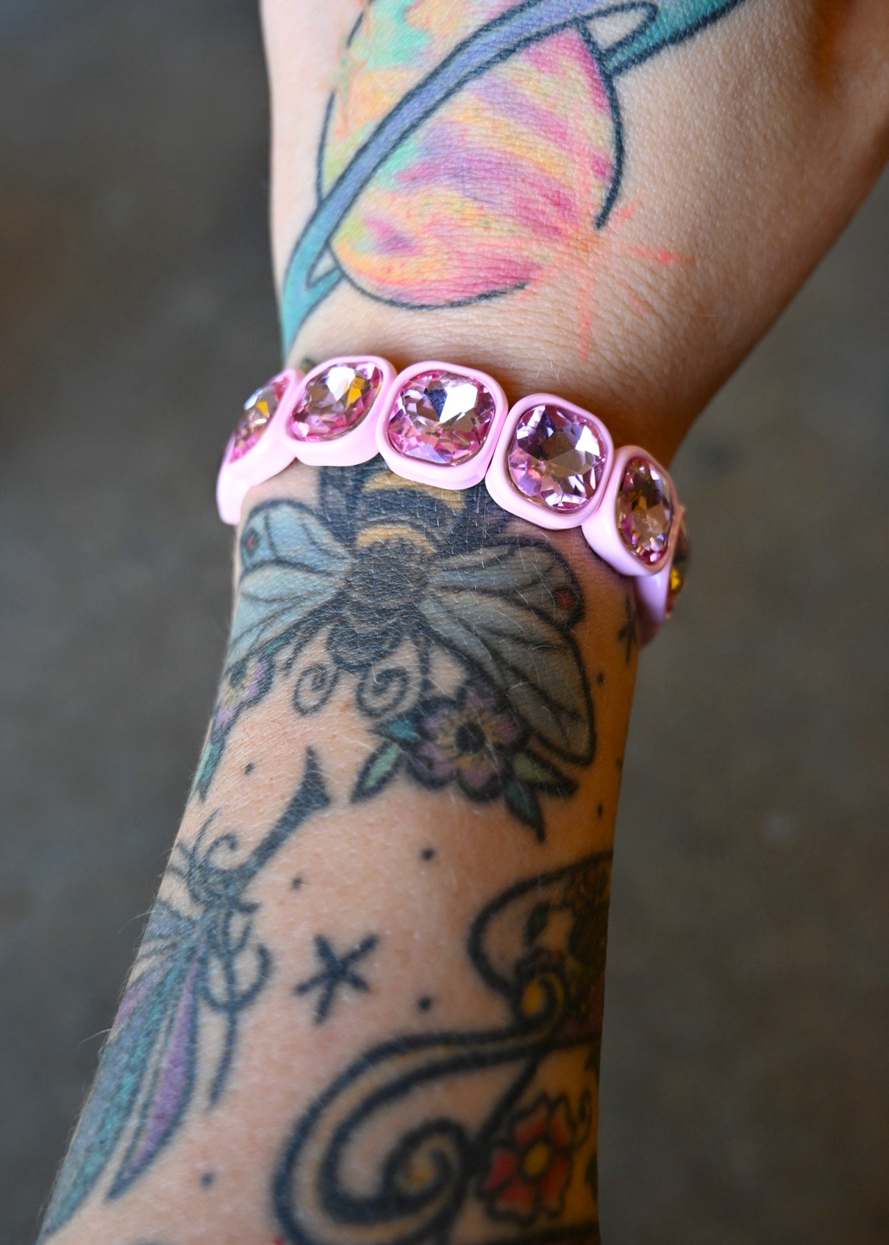 A model's wrist wearing a light pink gemstone bracelet on a dark background