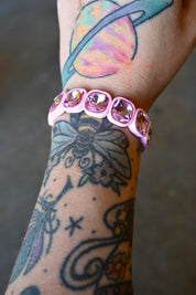 A model's wrist wearing a light pink gemstone bracelet on a dark background