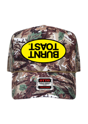 A camouflage trucker hat with a yellow oval 'BURNT TOAST' logo patch on the front and an OTTO patch on the brim, shown against a plain white background.