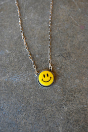 Close up of a silver chain necklace with a yellow smiley pendant on a dark background