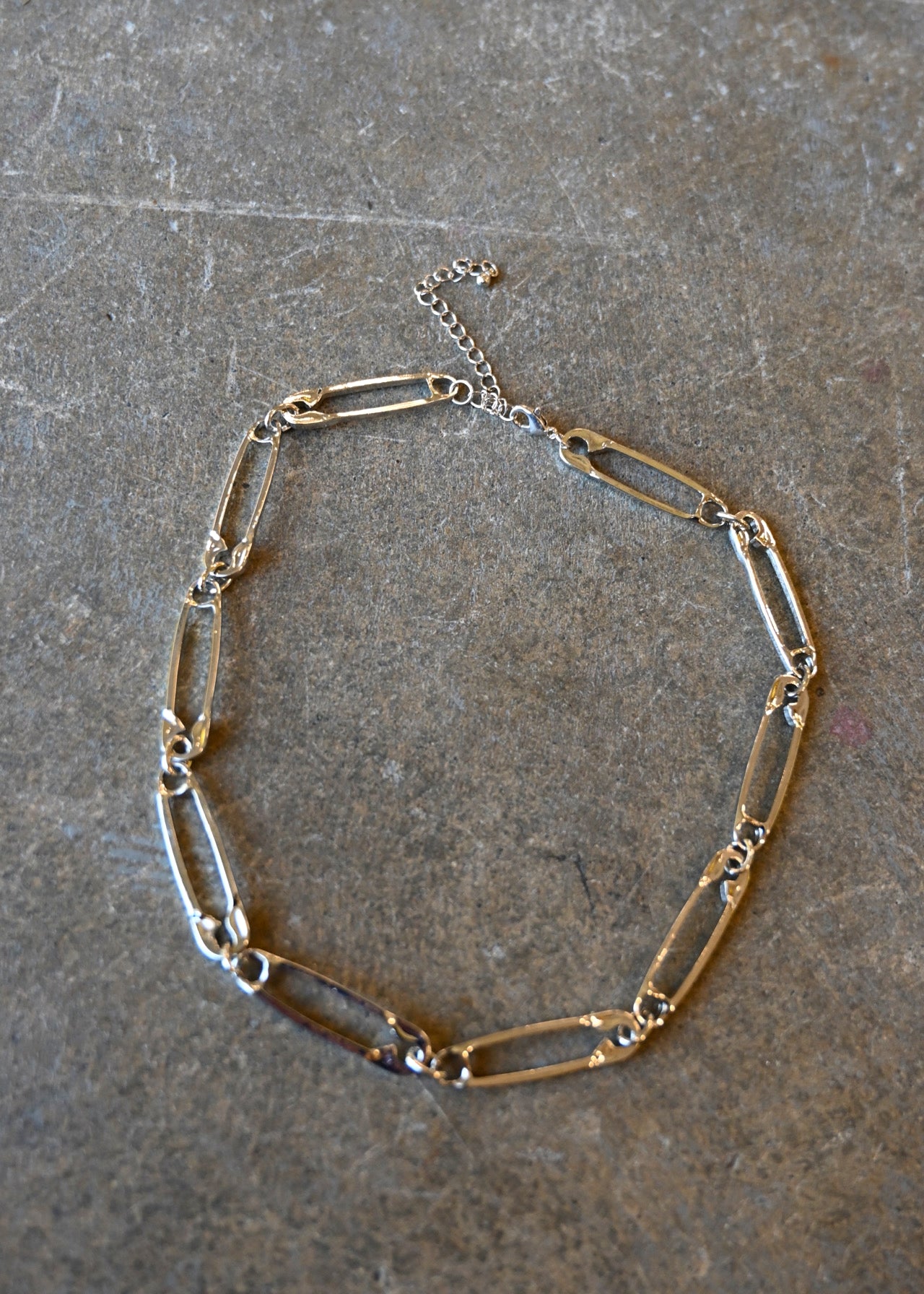 A silver necklace made of safety pins on a dark background