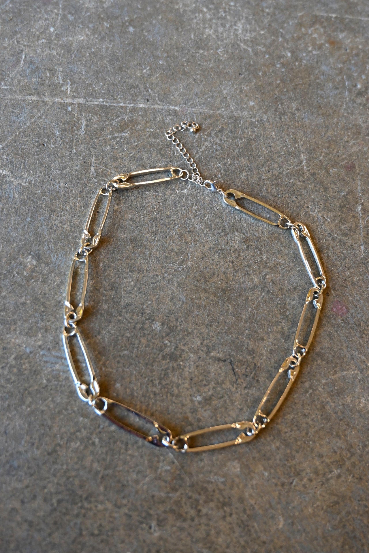 A silver necklace made of safety pins on a dark background
